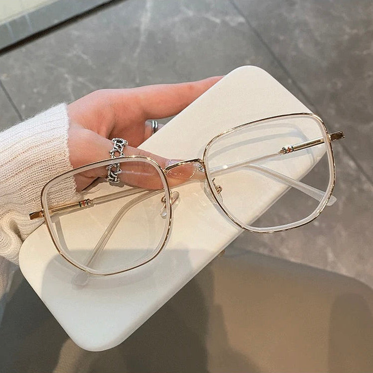 Gold-framed eyeglasses and case held by a hand over a neutral background