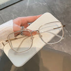 Gold-framed eyeglasses and case held by a hand over a neutral background