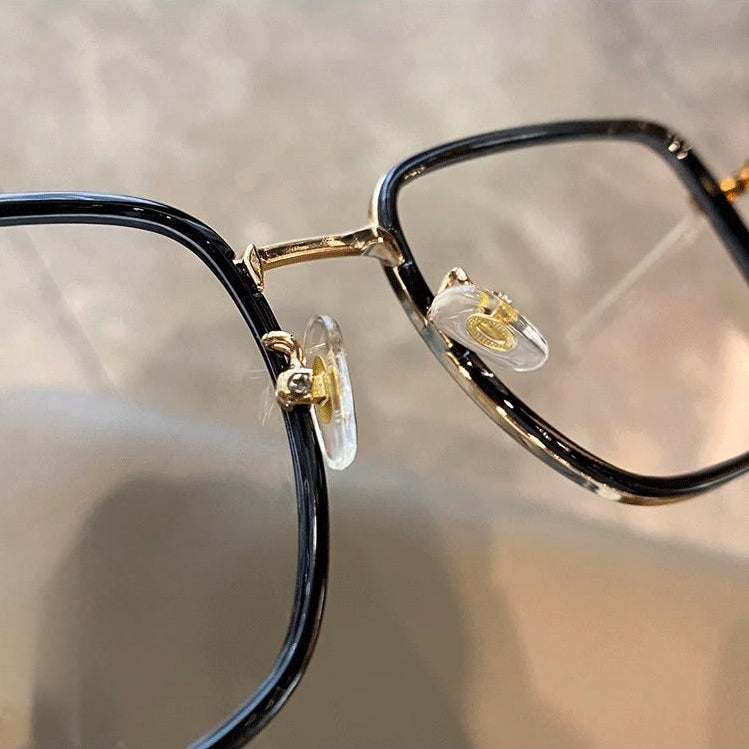 Close-up of a black-framed eyeglasses with gold accents on a blurred background