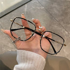 Hand holding a pair of black and gold eyeglasses against a neutral background